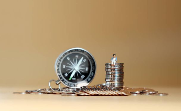 Eine Miniaturfrau sitzt mit einem Baby auf einem Haufen Münzen vor einem Kompass. - Foto, Bild