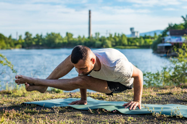 Een jongeman zit op een steengroeve meer bij de zon, yoga te doen. Zittend in yoga houding. Evenwicht, harmonie, concentratie en ontspanning. - Foto, afbeelding