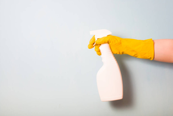 female hand in a yellow rubber glove holds a white spray bottle, spray bottle without a label on a light blue background, copy space - Fotoğraf, Görsel