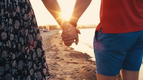 Primer plano de una pareja joven en vacaciones románticas tomados de la mano caminando en una playa vacía al atardecer, 4k cámara lenta
 - Metraje, vídeo