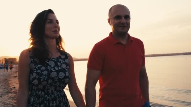 Fiatal pár romantikus nyaralás kéz a kézben sétálva egy üres strandon naplementekor, 4k lassított felvétel - Felvétel, videó