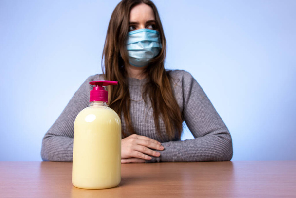 a young girl in a medical mask at a bottle with an antiseptic or cream in her hands. a disinfectant for treating bacteria. skin hydration. infection protection. quarantine precautions - Zdjęcie, obraz
