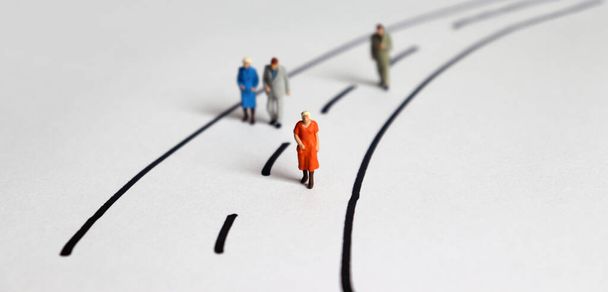Miniatuur oude mensen lopen op een tweesprong weg. Het concept van de samenleving op weg naar een vergrijzende samenleving. - Foto, afbeelding