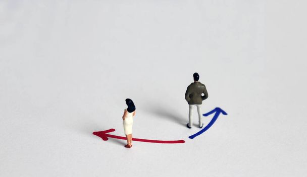 Ένας μικροσκοπικός άνδρας στέκεται μπροστά μπλε κατεύθυνση χρώμα με μια γυναίκα μινιατούρα στέκεται μπροστά κόκκινο χρώμα κατεύθυνση. - Φωτογραφία, εικόνα