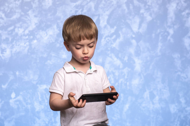 трирічна дитина обережно і з несподіванкою дивиться на смартфон. дитячі ігри. хлопчик дивиться мультфільми на планшеті. шкода від технології та радіації
. - Фото, зображення