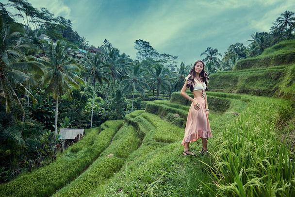 Hermosa chica en un vestido rosa con plumas en el pelo en una terraza de arroz, Bali
 - Foto, imagen
