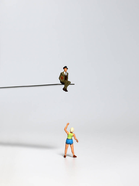 Ein Miniaturmann sitzt am Rande einer Klippe und eine Miniaturfrau gestikuliert mit der Hand. - Foto, Bild