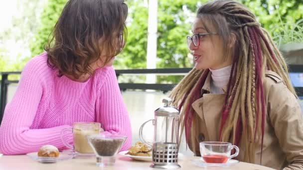 Twee jonge vriendinnen praten en drinken koffie en thee in het café op straat tijdens een lentedag. - Video
