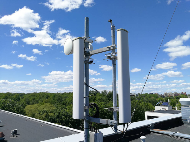 Estación base GSM (Global System for Mobile communication) y torre repetidora frente al cielo azul nublado para telecomunicaciones
 - Foto, Imagen