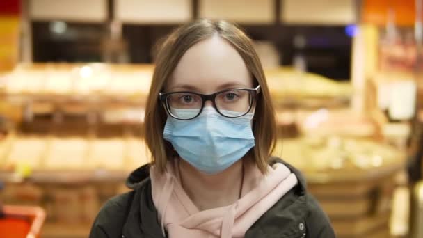 Donna in maschera protettiva medica e occhiali. Ritratto. Supermercato al rallentatore, primo piano. - Filmati, video