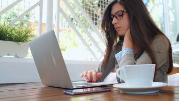 Красивая молодая успешная деловая женщина с ноутбуком в кафе пьет кофе, работает на ноутбуке, и с помощью телефона
. - Кадры, видео