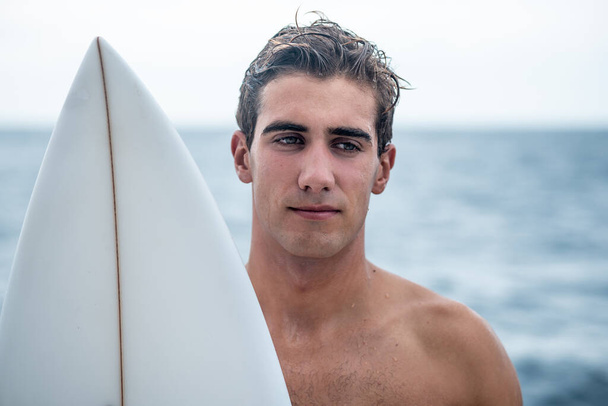 Portrait of young man, surfer with white surfboard and blue ocean on background - Foto, Imagen