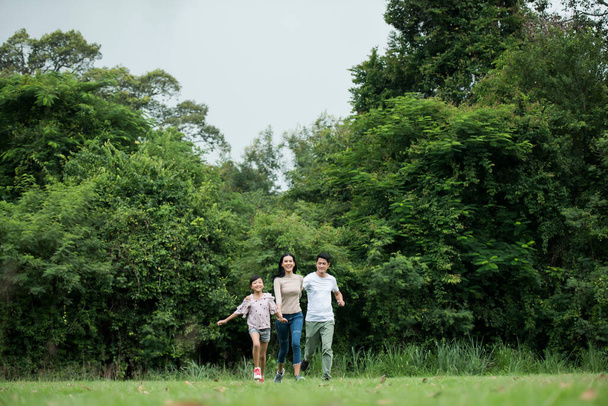 Ευτυχισμένη οικογένεια διασκεδάζει Μητέρα, πατέρας και κόρη τρέχουν στο πάρκο. - Φωτογραφία, εικόνα