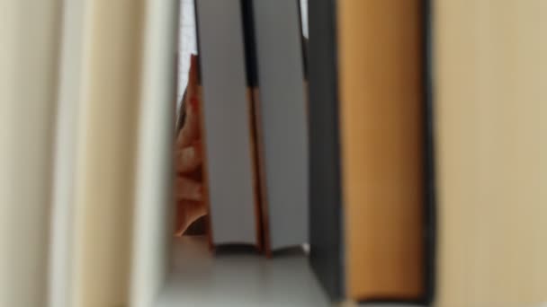 Mujer hermosa joven caucásica en gafas eligiendo un libro entre los estantes de libros en casa. 4k
 - Imágenes, Vídeo