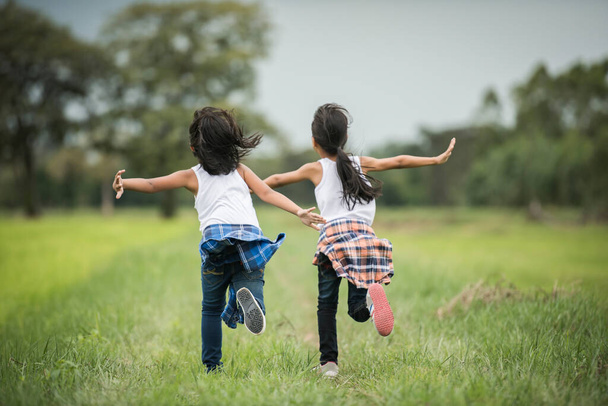 Two little cute girls are running on green grass. Best friends. - Foto, imagen