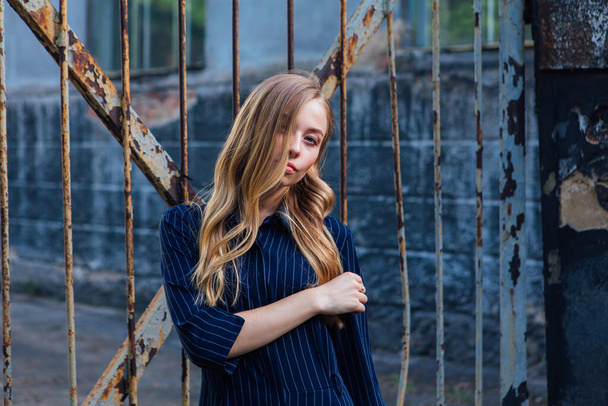 Close up portrait of a fashion look's woman with long blond hair standing near the old rusty gate. Young woman modern portrait. - Foto, Imagen