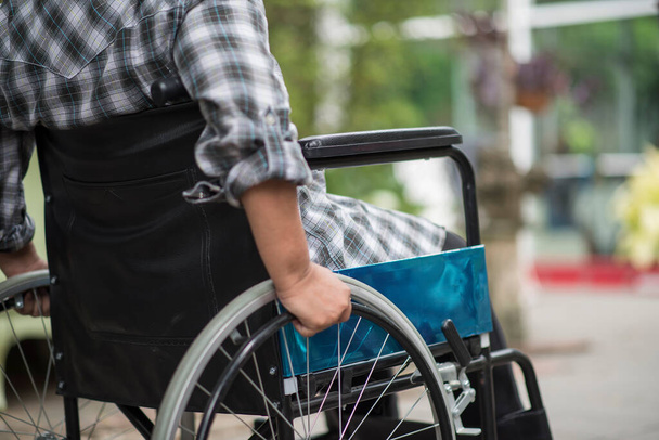 Κοντινό πλάνο της ηλικιωμένης γυναίκας χέρι στον τροχό της αναπηρικής πολυθρόνας κατά τη διάρκεια του περπατήματος στο νοσοκομείο - Φωτογραφία, εικόνα