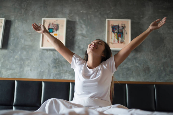 Boldog ázsiai fiatal nő nyújtózkodik, miután felébredt, míg a hálószobában - Fotó, kép