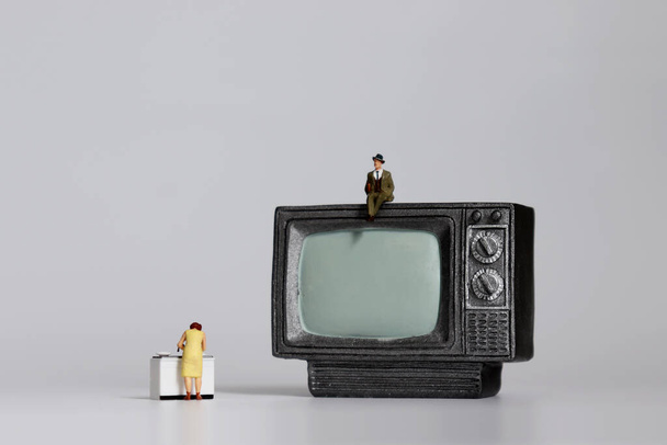 Homme miniature assis à la télévision et faisant la vaisselle avec une femme miniature. - Photo, image