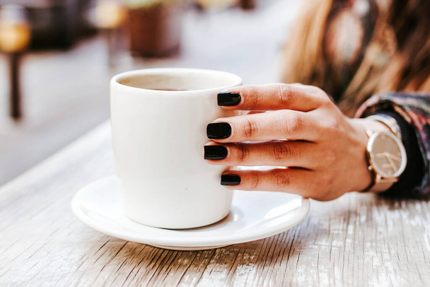 woman hand holding a cup of coffee outdoors at coffee shop or cafe with blurred background - Fotó, kép