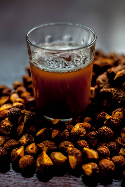 Close up shot of fresh raw soapnut on the brown surface along with its solution or liquid in a glass alongside it. - Photo, Image