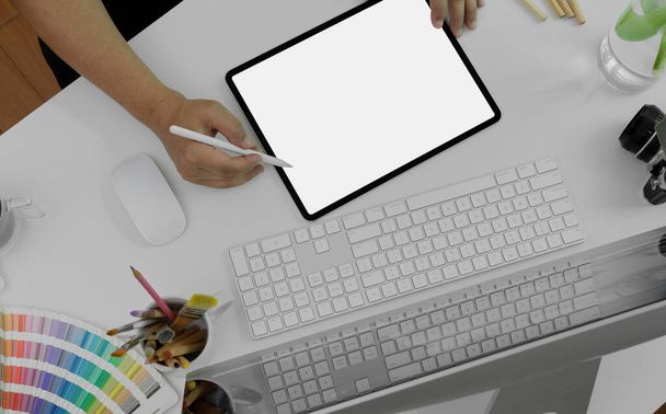Horní pohled na mužský grafický designér kreslící na maketový digitální tablet na bílém kancelářském stole s počítačem, fotoaparátem a designérskými potřebami  - Fotografie, Obrázek