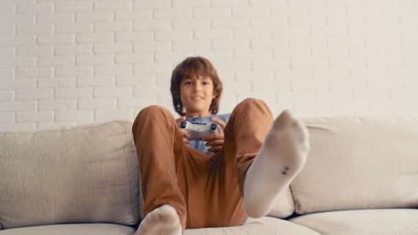 Młody, nastoletni chłopiec gra w konsolę do gier wideo, bawi się, śmieje, trzyma joysticka, 4k - Materiał filmowy, wideo