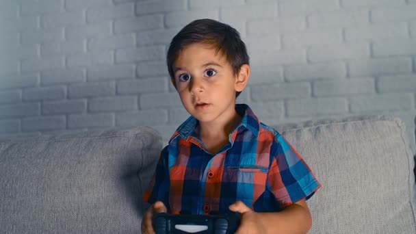 5歳の少年は、ビデオゲームコンソールをプレイし、家でジョイスティックを保持し、笑い、楽しみを持っている、 4k - 映像、動画