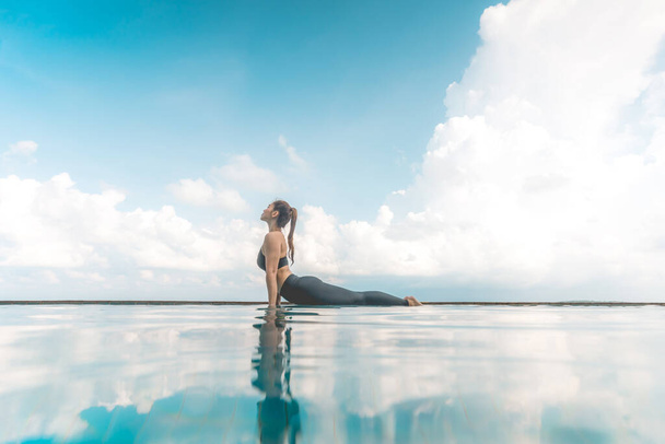 Vacation of Attractive Asian woman practice Cobra Pose on the pool above the beach in the morning with beautiful sea in Tropical island,Feeling comfortable and relax in holiday,Vacations Concept - Фото, изображение