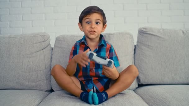 5歳の少年は、ビデオゲームコンソールをプレイし、家でジョイスティックを保持し、笑い、楽しみを持っている、 4k - 映像、動画