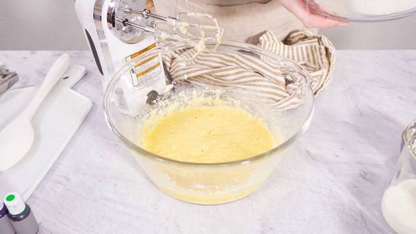 Paso a paso. Ingrediente de mezcla en un tazón de mezcla con una batidora eléctrica para hornear cupcakes de vainilla Mardi Gras. - Foto, Imagen