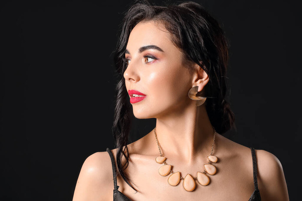 Beautiful young woman wearing stylish jewelry on dark background - Foto, Imagem