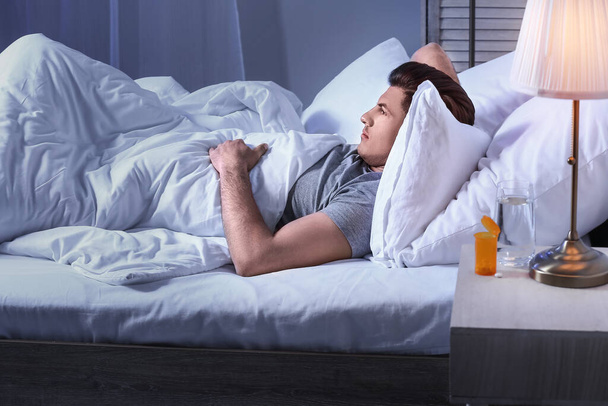 Молодой человек лежит в постели ночью
 - Фото, изображение