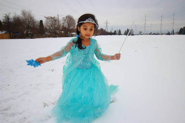 Een klein meisje in een prachtige blauwe jurk spelend in de sneeuw - Foto, afbeelding
