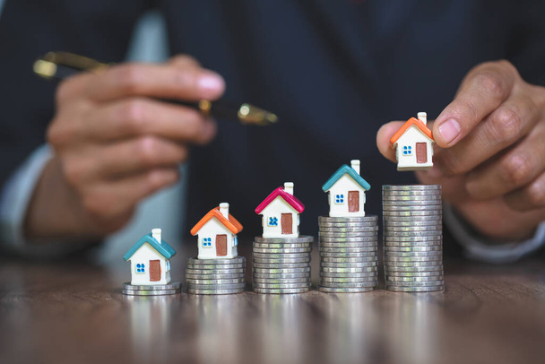 Woman hand hold a  home model put on the stack coin with growing, Savings money for buy house and loan to business investment for real estate concept. Invesment and Risk Management. - Photo, Image