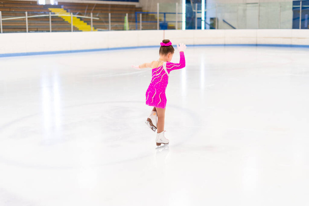 Kleine kunstschaatser in roze jurk aan het oefenen op de indoor ijsbaan. - Foto, afbeelding