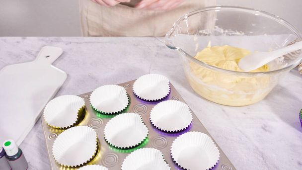 Askel kerrallaan. Scooping cupcake taikina folio cupcake vaipat leipoa vanilja Mardi Gras cupcakes. - Valokuva, kuva