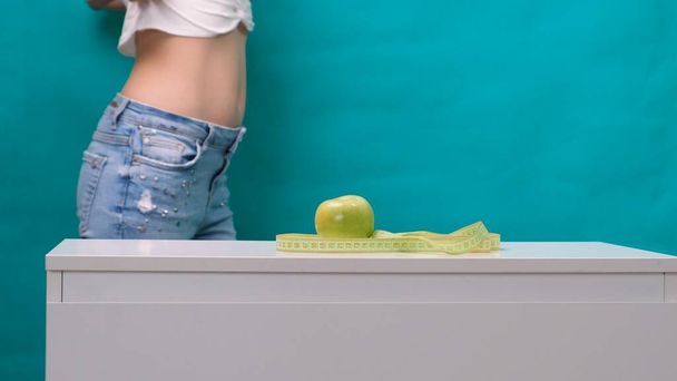 Kobieta odchudzony żołądek i zielone jabłko na pierwszym planie, selektywne skupienie. Pojęcie odchudzania i właściwego odżywiania - Zdjęcie, obraz