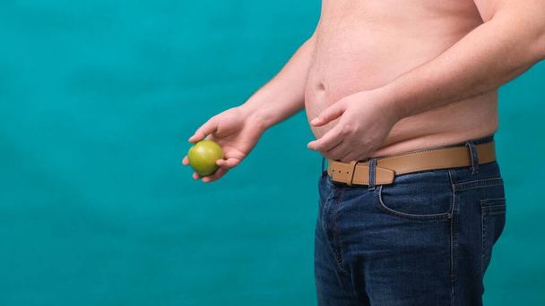 fat man with a big belly holds a green apple in his hand. The concept of healthy eating and losing weight, diet. - Photo, Image