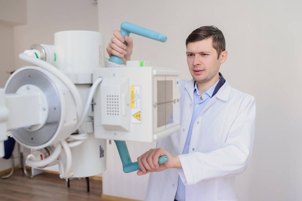  visión lateral de un radiólogo masculino ajustando la máquina de rayos X en el examen rom
 - Foto, Imagen