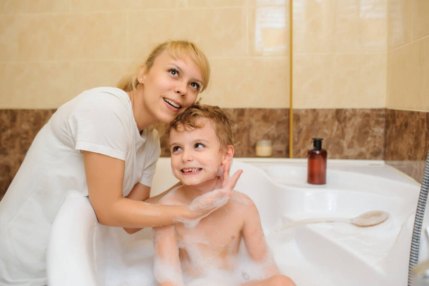 Little boy washing and playing in bathtub with foam and soap bubbles with his mother - Photo, Image