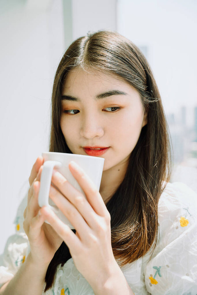 Belle asiatique jeune femme thai tenant tasse blanche de café chaud - Photo, image