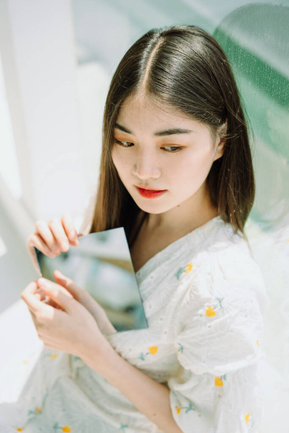 Hermosa asiática joven tailandesa sosteniendo placa de espejo con dos manos
. - Foto, imagen