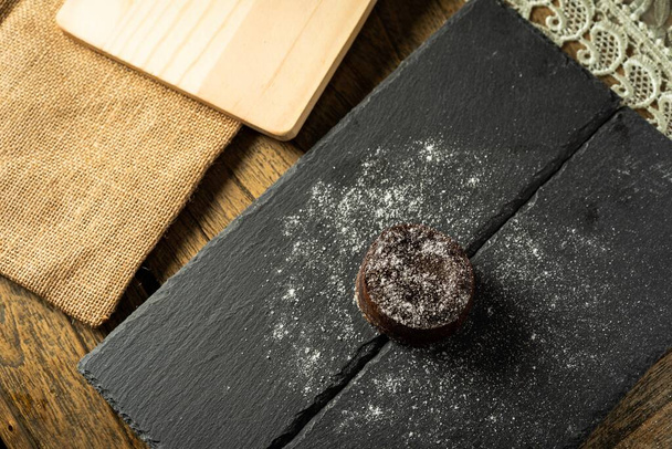 Chocolate fondant with icing sugars on top, on a black slate plate, selective focus - Photo, Image
