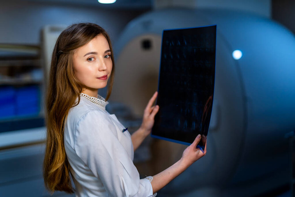Radiologist female doctor with x-ray picture in hands. CT machine on background. - Fotografie, Obrázek