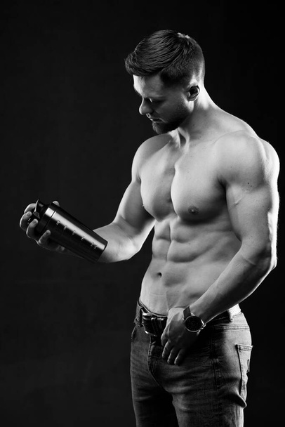 Very muscular sporty guy holding protein drink. Man with naked torso. Athletic body. Sport and sport nutrition concept. Black and white photo. - Zdjęcie, obraz