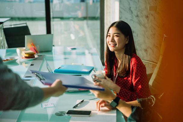 Красивая молодая азиатская тайская предпринимательница в красной рубашке в конференц-зале, работающая с деловыми людьми
. - Фото, изображение