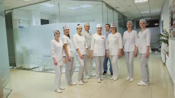 Μια ομάδα επαγγελματιών γιατρών με στολή διπλώνουν τα χέρια τους στο λόμπι μιας σύγχρονης κλινικής και χαμογελούν. - Πλάνα, βίντεο