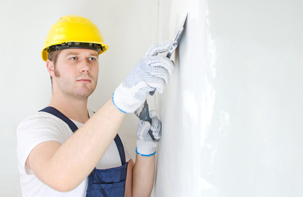 Male builder repairs wall with spackling paste - Foto, afbeelding