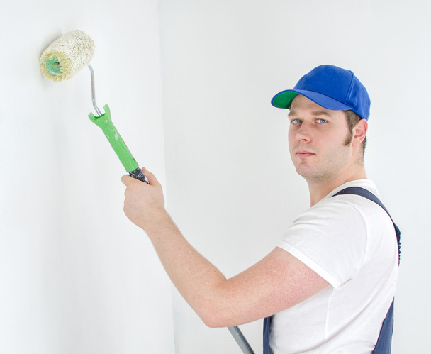 Painter in uniform paints the wall. - Φωτογραφία, εικόνα